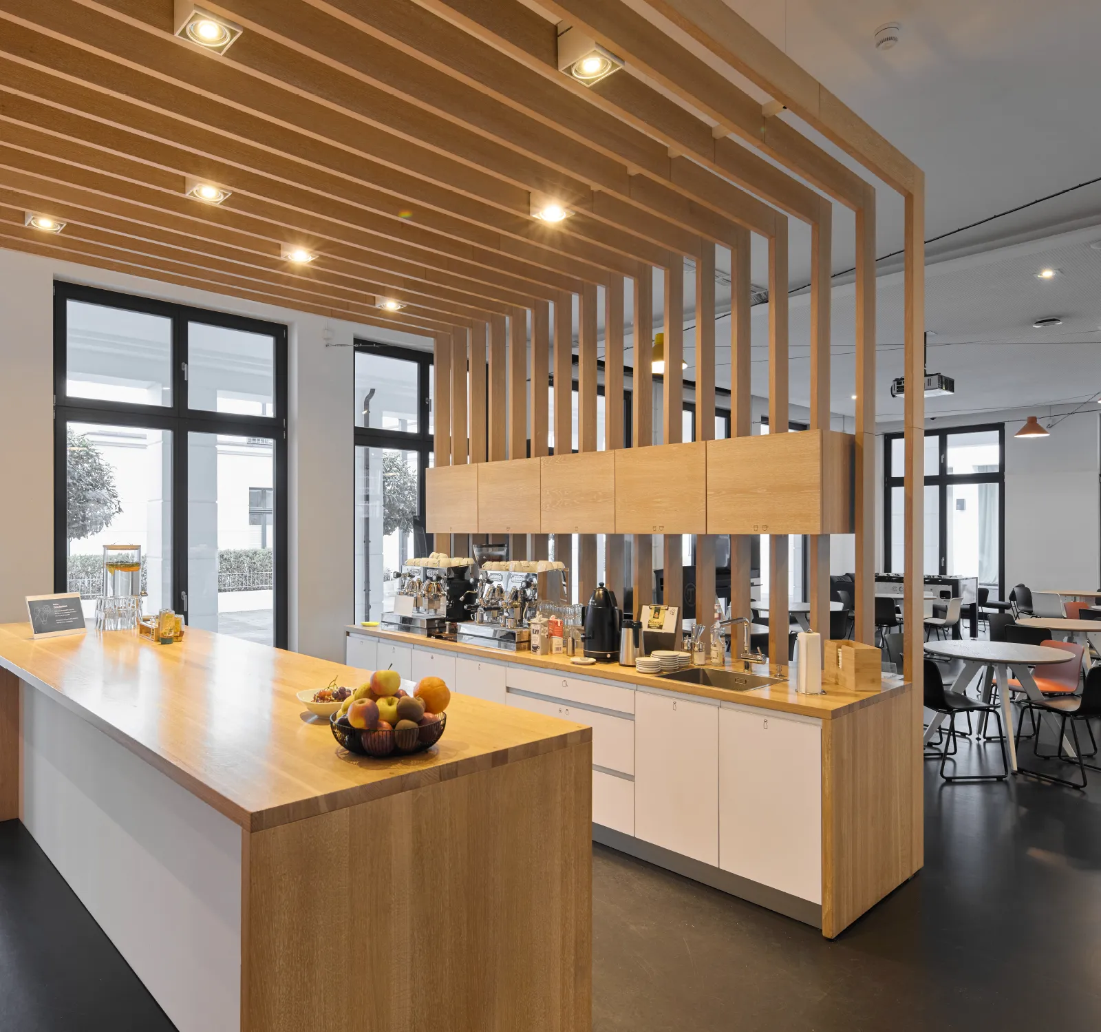 Moderne Küche im Haus A, Büroflächen Westend Ottensen, Hamburg, mit Holzregalen und einer Obstschale auf der Theke.