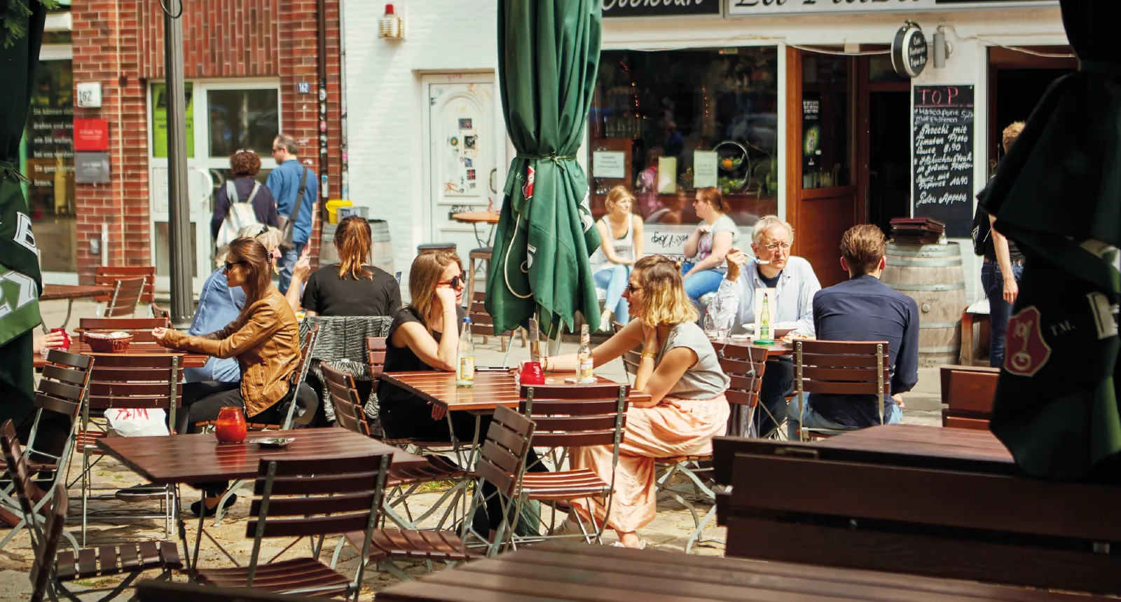 Besucher genießen die Sonne und Geselligkeit auf dem Ottensen-Markt in einem belebten Straßencafé.